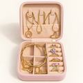 Open pink jewellery gift box with gold-tone necklaces, bangle, earrings and gemstone rings