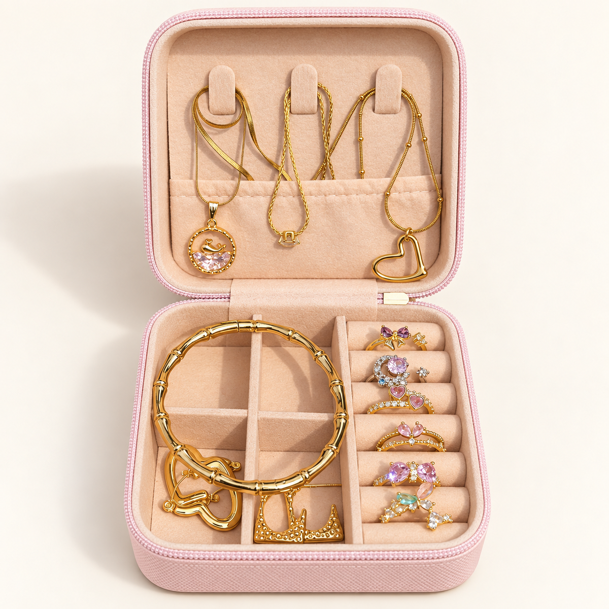 Open pink jewellery gift box with gold-tone necklaces, bangle, earrings and gemstone rings