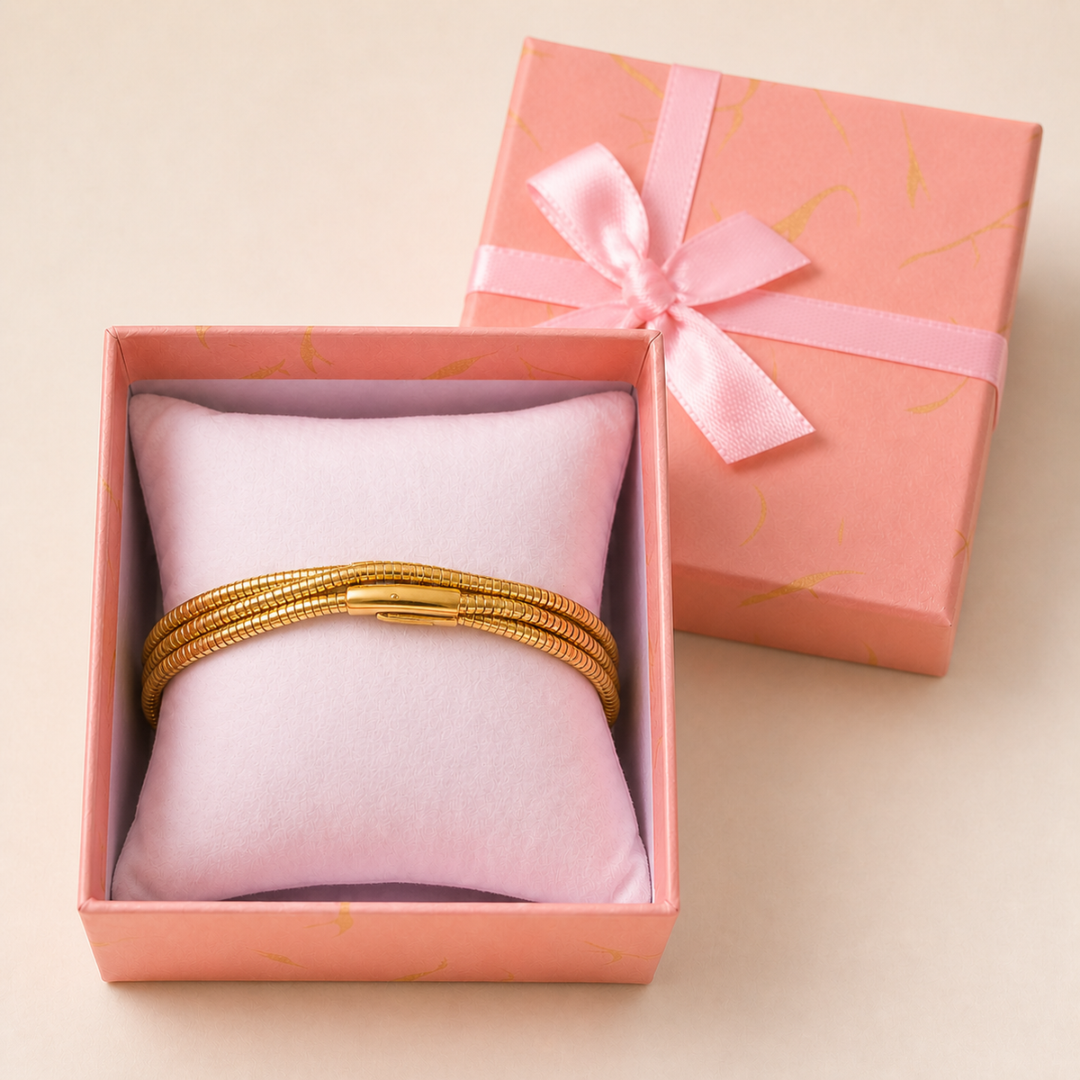 Triple-layer wrap snake Bracelet in an open blush-pink gift box — worn around the cushion